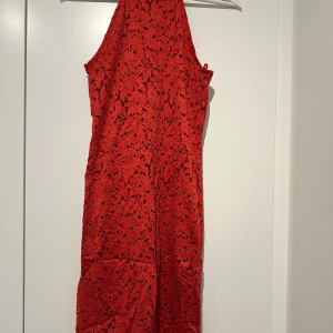 Röd spetsklänning - Snygg röd spetsklänning med ärmlös design och figurnära passform. Perfekt för en kväll ute eller en speciell tillställning. Klänningen har ett vackert blommigt mönster som ger en romantisk touch.