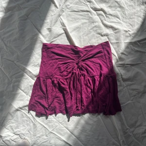 Vinröd tubtopp med knyt - Säljer en lila aktig tubtopp med knyt med en söt volangdetalj nedtill. blädra för bild med den på