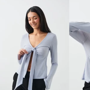 Ljusblå topp med knyt - Säljer en stilren ljusblå topp med knyt framtill. Toppen har en v-ringad design och långa ärmar, perfekt för en chic look. Passar bra till både jeans och kjol.