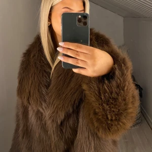 Brun pälsjacka - Säljer en lyxig brun pälsjacka med en elegant och fluffig design. Jackan har långa ärmar och en generös krage som ger en glamorös look. Perfekt för att hålla sig varm och stilfull under kalla dagar. Ganska tunn!
