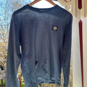 Blå långärmad tröja från Stone Island - Snygg blå långärmad tröja från Stone Island med logga på bröstet. Perfekt för en stilren och avslappnad look. Storlek S men passar även mig som har M