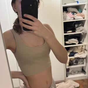 Beige ribbad linnetopp från Gina Tricot - Säljer en snygg beige ribbad linnetopp från Gina Tricot. Toppen är ärmlös och har en tight passform, perfekt för varma dagar. Den är gjord i ett mjukt och stretchigt material som sitter skönt mot kroppen. Perfekt för en stilren och enkel look.