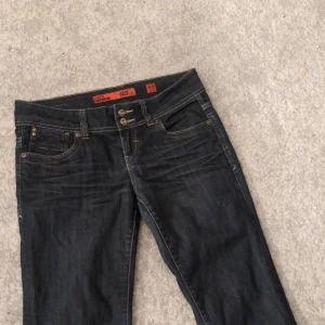 Mörkblå jeans från QS by s.Oliver - Snygga mörkblå jeans från QS by s.Oliver med klassisk femficksdesign och dubbla knappar i midjan. Perfekta för en avslappnad stil.