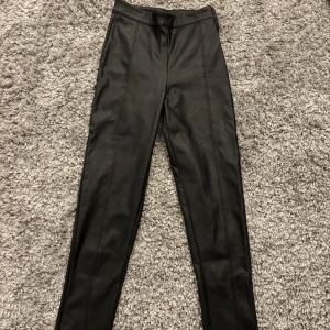 Svarta skinnbyxor från Gina Tricot - Snygga svarta skinnbyxor från Gina Tricot i storlek XXS. Byxorna har en tight passform och dragkedja i midjan. Perfekta för en stilren look.