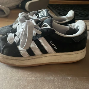 Svarta Adidas Campus sneakers - Säljer ett par klassiska svarta Adidas Campus sneakers. De har lite defekter som man kan se fatmföralkt där bak men även lite slitage framgår. De är köpta för 1500 och jag säljer nu för 500kr!