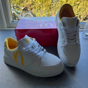 Vita sneakers med McDonald's tema - Unika vita sneakers med McDonald's tema. Skorna har gula detaljer och McDonald's logga på tungan samt texten 'I'm lovin' it' på hälen. Skorna är limited edition och går ej att få tag i. Storlek 42🍔👌🏼😍