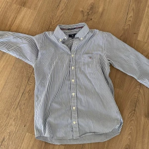 Randig skjorta från GANT - Säljer en stilren blå- och vitrandig skjorta från GANT. Skjortan har långa ärmar hade den när jag va lite så de är anledningen till varför jag säljer den