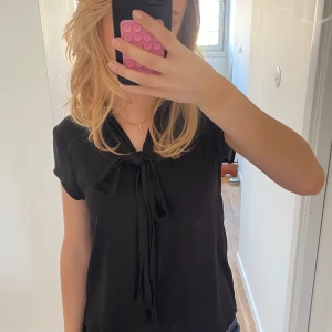 Svart blus med knytband - Snygg svart siden blus med korta ärmar och ett knytband vid halsen. 