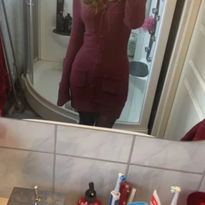 Vinröd stickad klänning med knappar - Snygg vinröd stickad klänning med knappar framtill och fickor. Använd 1 gång!