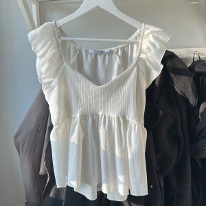 Vit ärmlös topp med volangdetaljer - Säljer en söt vit ärmlös topp från 157 med volangdetaljer vid axlarna. Toppen har en lätt ribbad struktur och en luftig passform som passar perfekt för varma dagar. Perfekt för en somrig look! 🌞endast testad