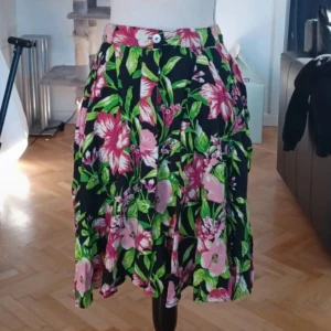 Blommig kjol från Forever 21 - Säljer en färgglad blommig kjol från Forever 21. Kjolen har ett härligt mönster i rosa och grönt på en svart bakgrund. Den saknar en knapp i midjan och är perfekt för sommarens alla tillfällen. 🌸