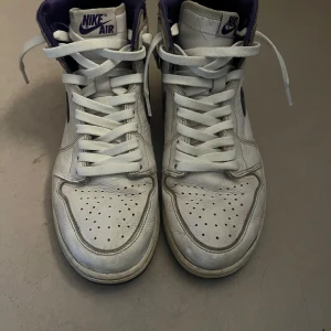 Jordan retro 1 high purple  - Snygga Nike Air sneakers i vitt med lila detaljer. Skorna har klassisk snörning och en hög design som ger extra stöd. Perfekta för dig som vill ha en stilren look med en touch av färg.