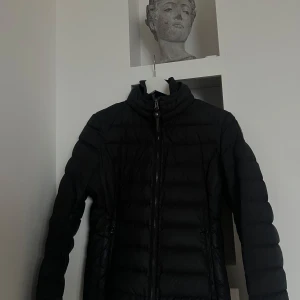 Svart dunjacka från Parajumpers - Säljer en svart dunjacka från Parajumpers med en cool patch på ärmen. Jackan har en dragkedja framtill och den är superlätt. Perfekt för kyliga dagar när du vill hålla stilen. 🖤