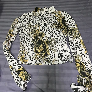 Mönstrad långärmad topp från Gina Tricot - Säljer en cool långärmad topp från Gina Tricot med leopardmönster och barockinspirerade detaljer i svart och guld. Perfekt för att sticka ut med stil! 🖤✨