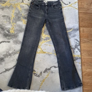Grå bootcut jeans från Gina Tricot - Snygga grå bootcut jeans från Gina Tricot. De har en klassisk femficksdesign och stängs med knapp och dragkedja. Perfekta för en stilren look.