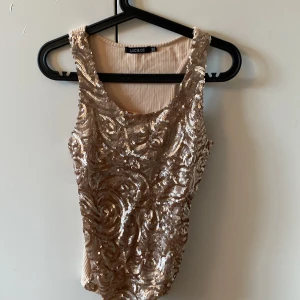 Beige paljettlinne från LUC & CE - Säljer ett snyggt beige linne från LUC & CE med glittriga paljetter på framsidan. Linnet har en ribbad baksida och är ärmlöst, perfekt för en festlig look. Passar utmärkt till både jeans och kjol.