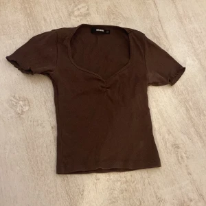 Brun ribbad topp från Bik Bok - Säljer en brun ribbad topp från Bik Bok i storlek XS. Toppen har en v-ringad design och korta ärmar, perfekt för en stilren look. Passar bra till både jeans och kjol.