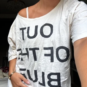 Vit t-shirt från Études - Säljer en vit t-shirt från Études med texten 'OUT OF THE BLUE' i svart. T-shirten har en loose passform och korta ärmar. Perfekt för vardag eller till ett par spetsbyxor för fest