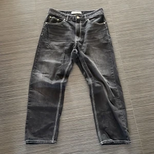 Svarta baggy jeans från Bershka - Snygga svarta baggy jeans från Bershka med kontrasterande vita sömmar. Byxorna har en klassisk femficksdesign och en knappgylf. Perfekta för en stilren look.