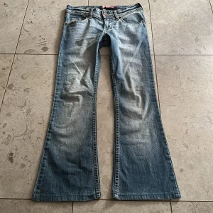 Lågmidjade bootcut jeans  - Så snygga lågmidjade vintage bootcut jeans med broderade detaljer på bakfickorna. Jeansen har en klassisk femficksdesign och knappgylf. Perfekta för en avslappnad stil med en touch av elegans. Midjemått tvärsöver: 33 cm. Innerbenslängd: 70 cm. De är för korta på mig så passar någon som är ca 153-155 cm.