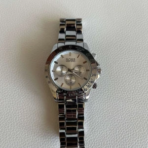 Silverfärgad klocka från Boss - Snygg och stilren silverfärgad klocka från Boss med metallarmband och flera urtavlor. Klockan har en klassisk design med tydliga markeringar och en robust känsla. Perfekt för den som gillar en elegant accessoar. Klockan är perfekt för den som vill sticka ut jämfört med andra. Klockan säljs för 900 kr 