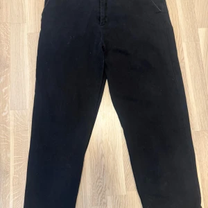 Svarta byxor från Studio Total - Snygga svarta byxor från Studio Total med en klassisk design. De har en knapp och dragkedja framtill samt hällor för bälte. Perfekta för en stilren look.