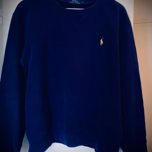 Mörkblå tröja från Ralph Lauren - Säljer en klassisk mörkblå tröja från Ralph Lauren med rund hals och det ikoniska logotypbroderiet på bröstet. Perfekt för en stilren och avslappnad look. Passar bra till både jeans och chinos.