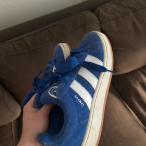 Blå Adidas Campus sneakers - Snygga blå Adidas Campus sneakers i mocka med vita detaljer och snörning. Perfekta för en avslappnad stil med klassiska tre ränder på sidan och Adidas-logga på hälen. Använda 3 gånger men tecken på användning finns, lite noppriga men går nog lätt bort storlek 40 2/3