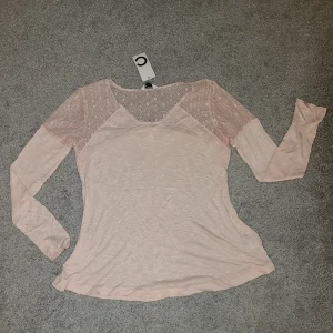 Rosa spetsdetaljerad topp - Säljer en söt rosa topp med spetsdetaljer på axlar och ärmar. Toppen har en mjuk och bekväm passform med långa ärmar. Helt ny, prislappen kvar. Köptes för 179kr. 