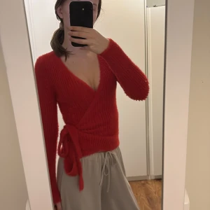 Röd omlottkofta - Säljer en snygg röd omlottkofta med knytband i midjan. Koftan är stickad och har en v-ringad design med långa ärmar. Väldigt gosig, varm och mjukt material. Storlek S. ❤️