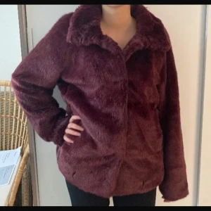 Vinröd pälsjacka - Säljer en snygg vinröd pälsjacka från Lindex. Jackan har en mjuk och fluffig yta med långa ärmar och knappar framtill. Perfekt för att hålla sig varm och stilren under kyliga dagar. Köptes för ca 850kr💕