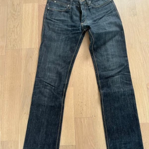 Mörkblå jeans från Acne - Snygga mörkblå jeans från Acne med klassisk femficksdesign och en läderpatch med logga baktill. Perfekta för en stilren look. Litet hål bak vid knäveck.