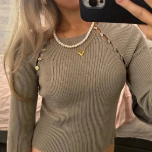 Beige ribbad tröja med knappar - Säljer en beige khaki ribbad tröja med dekorativa knappar längs axlarna. Tröjan har en tight passform och långa ärmar, perfekt för en stilren look. Från zara som inte säljs längre, storlek L men är väldigt liten i storlek passar mig som har xs-s💕