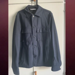 Mörkblå overshirt  - Snygg mörkblå overshirt från Acne Studios med knappar framtill och två stora bröstfickor. Perfekt för lager-på-lager-stil. Klassisk krage och långa ärmar ger en stilren look.