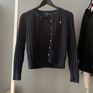 Mörkblå kofta från Ralph Lauren - Säljer en elegant mörkblå kofta från Ralph Lauren med kabelstickat mönster. Koftan har långa ärmar och knappar. Perfekt för en stilren look. Säljer för den har blivit lite liten.💕