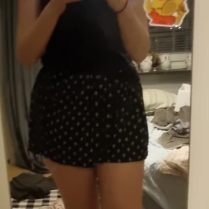 Svarta shorts med blommigt mönster från BikBok - Säljer en söt svart shortsl från BikBok med ett fint blommigt mönster i vitt. Kjolen har en lös passform och är perfekt för en avslappnad stil. Passar bra till både vardag och speciella tillfällen. 🌸