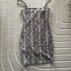 Ormmönstrad klänning - Snygg ormmönstrad klänning med smala axelband. Perfekt för en trendig look. Klänningen har en tight passform och är knälång.