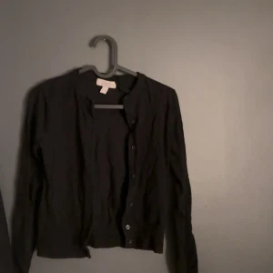 Svart kofta från H&M - Säljer en stilren svart kofta från H&M. Den har långa ärmar och knappar framtill. Perfekt för lager-på-lager under kyligare dagar. Passar till många olika outfits!