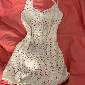 Vit stickad strandklänning - Säljer en söt vit stickad klänning köpt i ayia napa med ett vackert spetsmönster. Klänningen är ärmlös med smala axelband och har en kort längd som passar perfekt för stranden. Passar xs/s