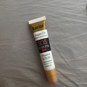 Karité SOS Lip Plump Serum - Enbart testats. Karité SOS Lip Plump är ett läppserum med arganolja och hyaluronsyra som återfuktar och ger fylligare läppar. Tuben är guldig och vit med svart och röd text samt en illustration av läppar. Innehåller 17 ml.