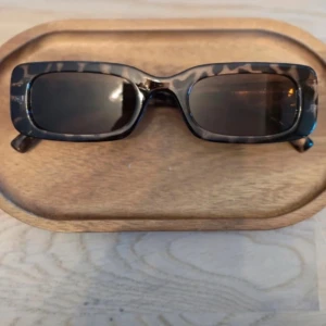 Rektangulära solglasögon med leopardmönster - Snygga solglasögon med rektangulära bågar i leopardmönster. Glasen är mörka och ramen har en trendig, kantig form som ger en cool look. Perfekt accessoar för att lyfta din stil.