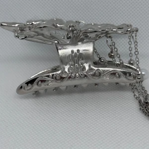 Silverfärgad hårklämma med fjärilsdesign och kedjor - Säljer en snygg silverfärgad hårklämma i form av en fjäril. Klämman har dekorativa kedjor med pärlor som hänger ner och ger en unik look. Perfekt accessoar för att lyfta din frisyr.
