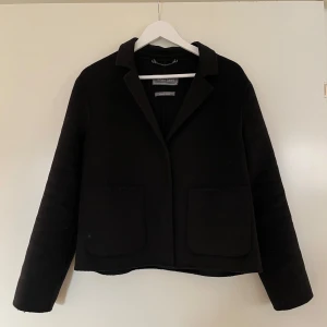Jacka, White Label, svart, 40 - Jacka/kort kappa från White Label (rofa fashion group) i storlek 40. Handgjord. 70% polyester och 30% ull. Knäpps med 3 osynliga knappar (se bild). 2 fickor fram. Kappan är i nyskick.  Mått: Längd ca 60 Armhåla till armhåla ca 50 Ärmlängd mätt från axel ca 58 Axelmått ca 46