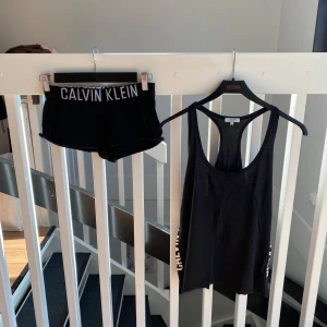 Set från Calvin Klein - Set från Calvin Klein. Linne med djup urringning och logga längs sidan. Tunt och luftigt material, perfekt för varma dagar eller träning. Shorts i samma material