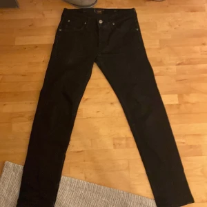 Svarta jeans från Lee - Säljer ett par svarta jeans från Lee med klassisk femficksdesign och raka ben. Jeansen har silverfärgade knappar och Lee-logga i midjan. Perfekta för dig som gillar en tidlös och enkel stil.