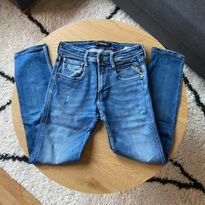 Klassiska Blåa Replay jeans  - Tjena👋 Säljer ett par klassiska blå jeans från Replay i Anbass modell med snygga slitningar och raka ben👖  Jeansen har fem fickor, dragkedja och knapp i midjan samt Replay-läderpatch bak. Perfekta för dig som gillar en tidlös jeanslook⏳  Väldigt najs material utan några defekter!🙌  Storleken är W28 L32📏  Men sitter som L30📐  Priset kan diskuteras vid snabb affär!💸  Vid minsta frågor: Meddela!📩