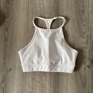 Vit sport-bh från Better Bodies - Säljer en vit sport-bh från Better Bodies med brottarrygg och hög halsringning. Perfekt för träning och ger bra stöd. Mjukt och stretchigt material som sitter skönt på kroppen.