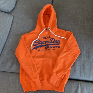 Superdry Hoodie - Säljer denna riktigt snygga orangea superdry hoodie. Har blivit använd fåtal gånger. Utan defekter!