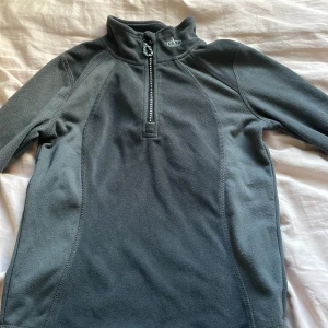 Grå fleece-tröja med dragkedja från Kingsland - Mysig grå fleece-tröja från Kingsland Equestrian med halv dragkedja framtill dekorerad med stenar. Broderad krona på bröstet och hög krage. Perfekt för ridning eller som ett extra lager under kyliga dagar. Orginal pris runt 1000kr. ⚠️Pris kan diskuteras ⚠️