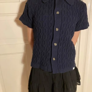 Mörkblå stickad kortärmad kofta från Les Deux - Säljer en mörkblå stickad kofta från Les Deux med korta ärmar och kabelstickat mönster. Koftan har knappar framtill och en klassisk krage. Perfekt för lager-på-lager och snygg till både jeans och kjol! Passar till både festligheter och vardag! 🥰💕